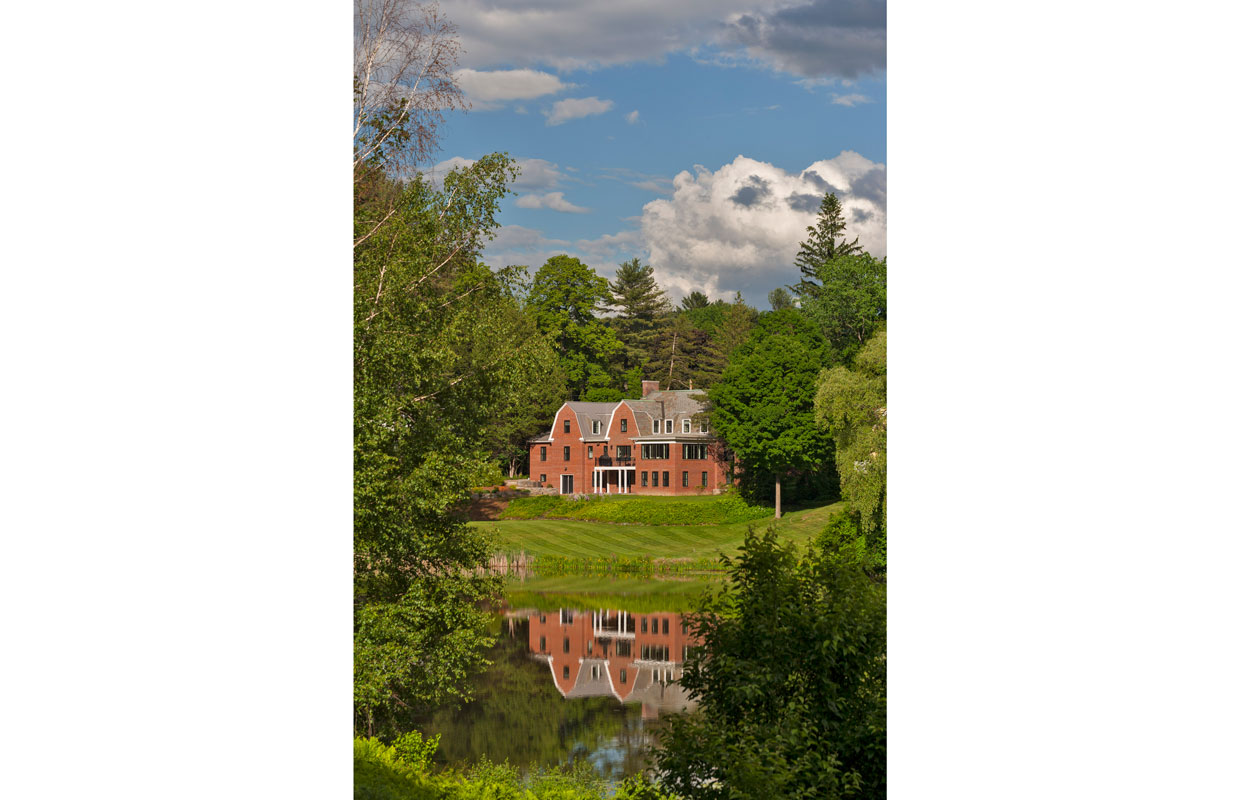 large brick house from a distance across a pond