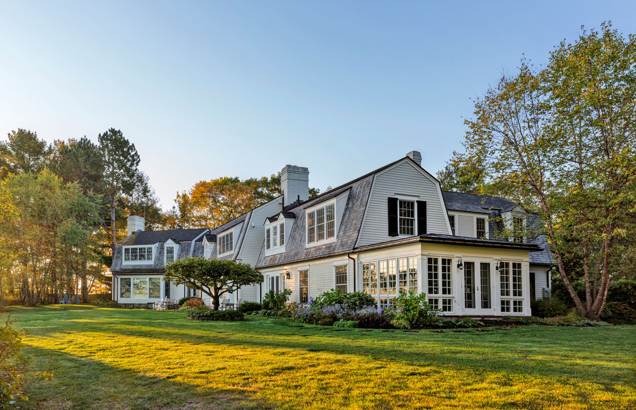 large gambrel white house with a black roof and a lush green yard