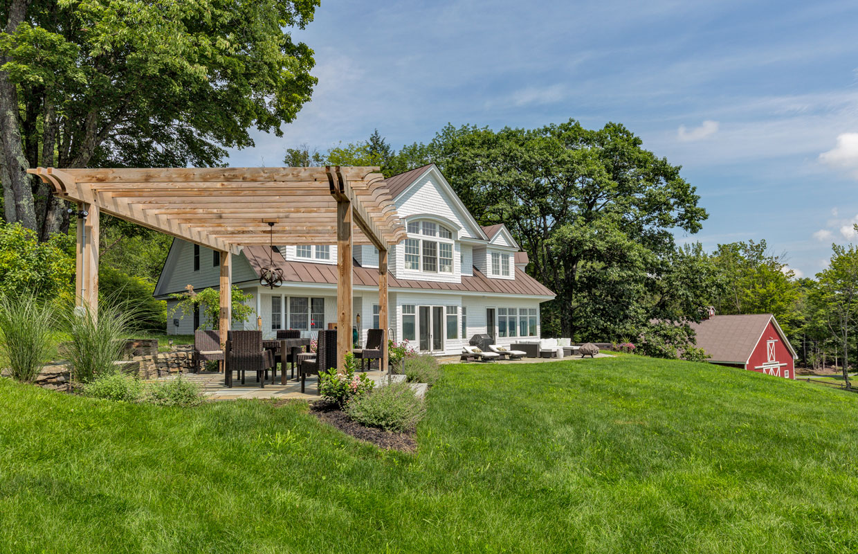 pergola with a large white house in the background and lush green grass