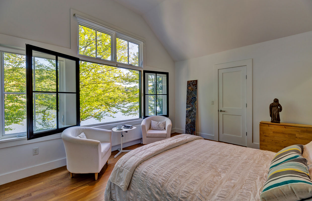 bedroom with large windows open to a lake view outside