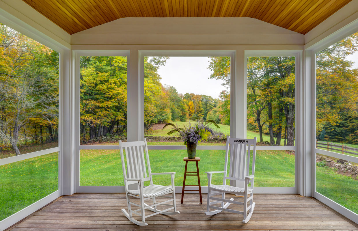 2 white rocking chairs on an outside covered deck with green grass in the background