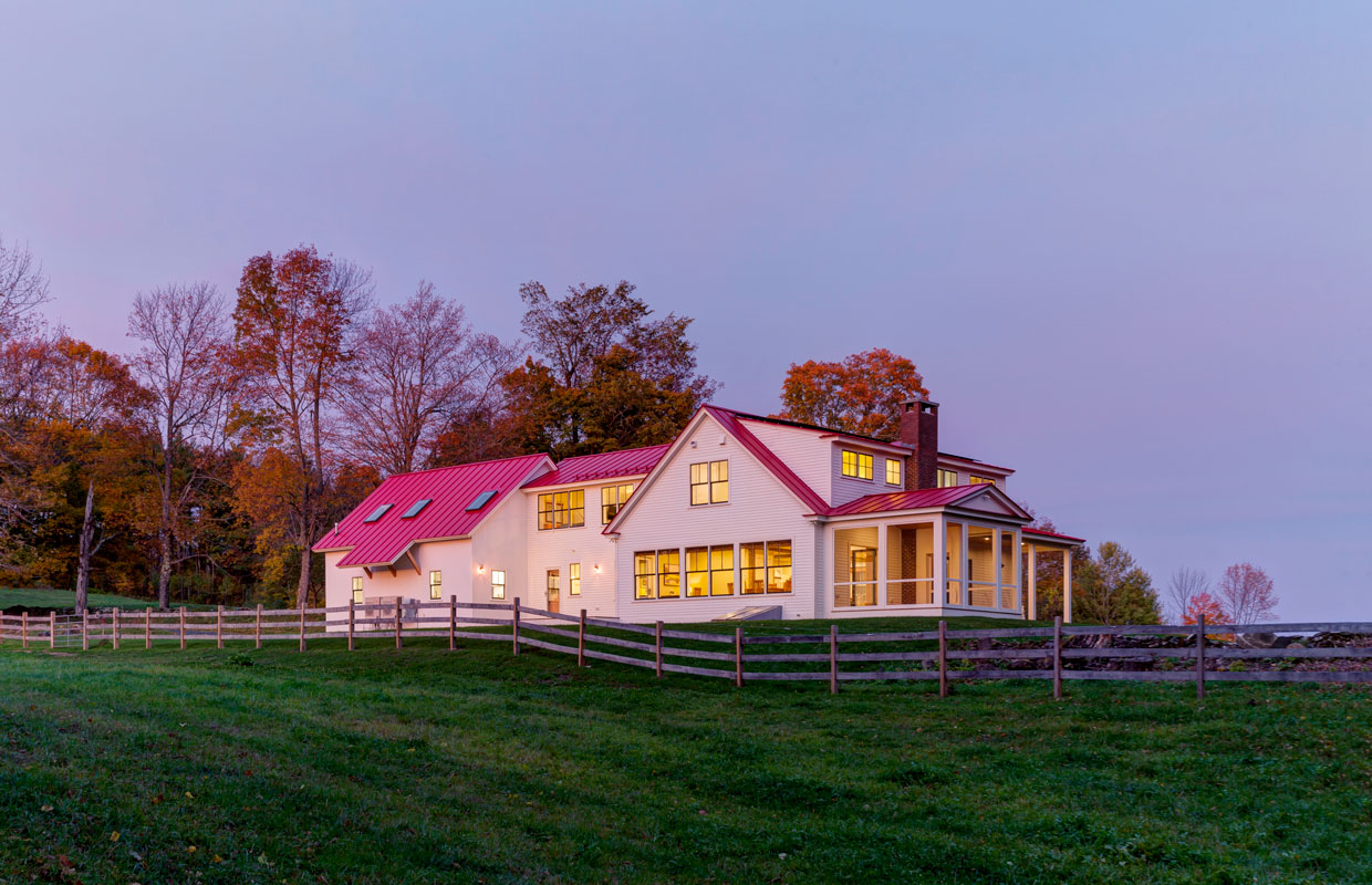 white house with a red roof with a large yard and wooden fence at dusk