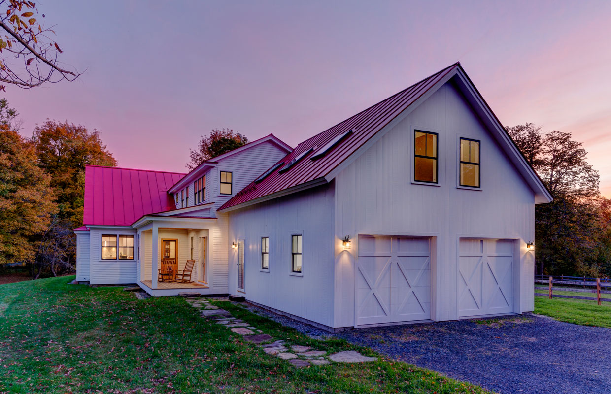 view from the garage of a large white house with a red roof at dusk