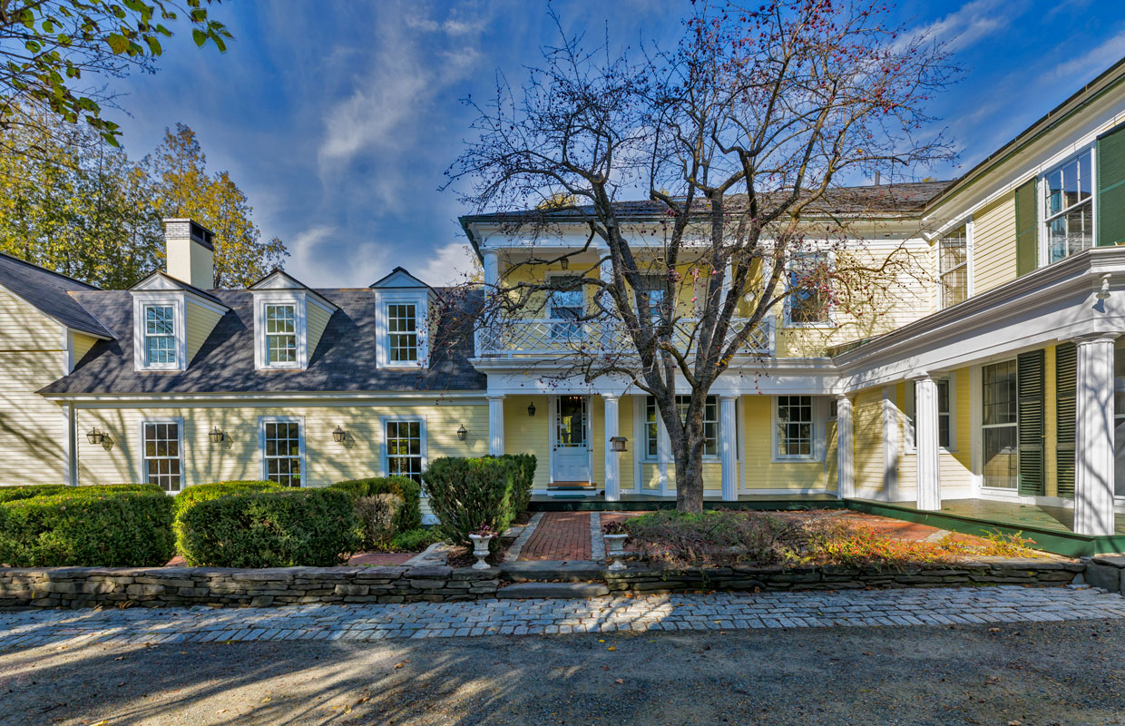 large yellow house with a tree and scrubs out front