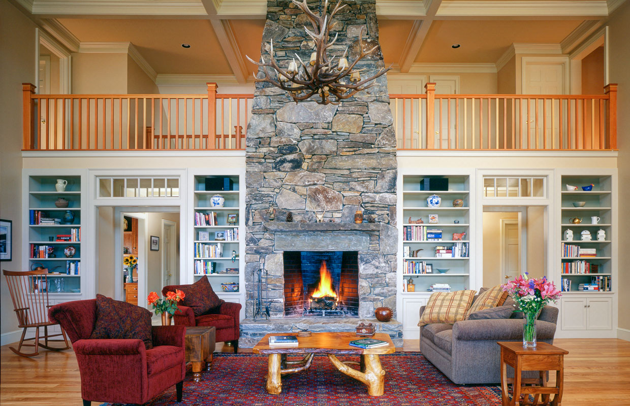 great room with a large fireplace and stone chimney in the center and a balcony behind