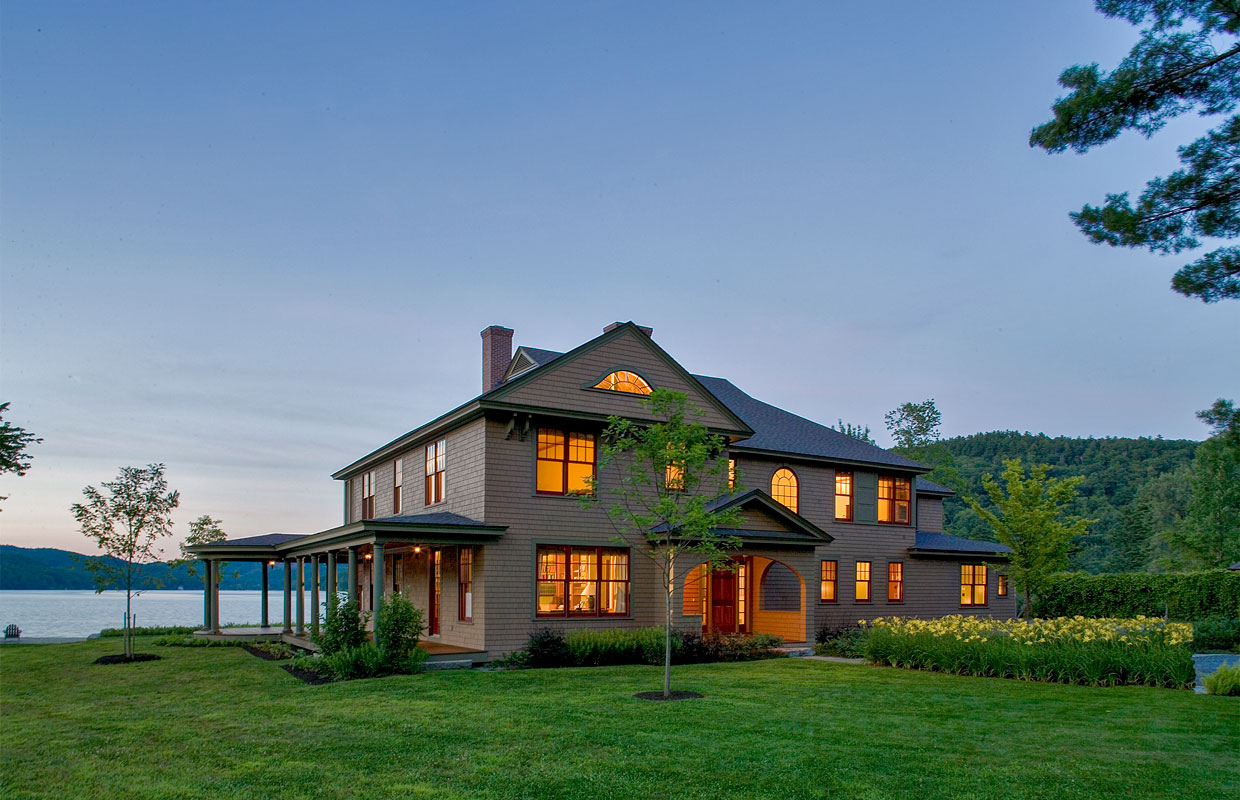 large lake house at dusk with lights on inside