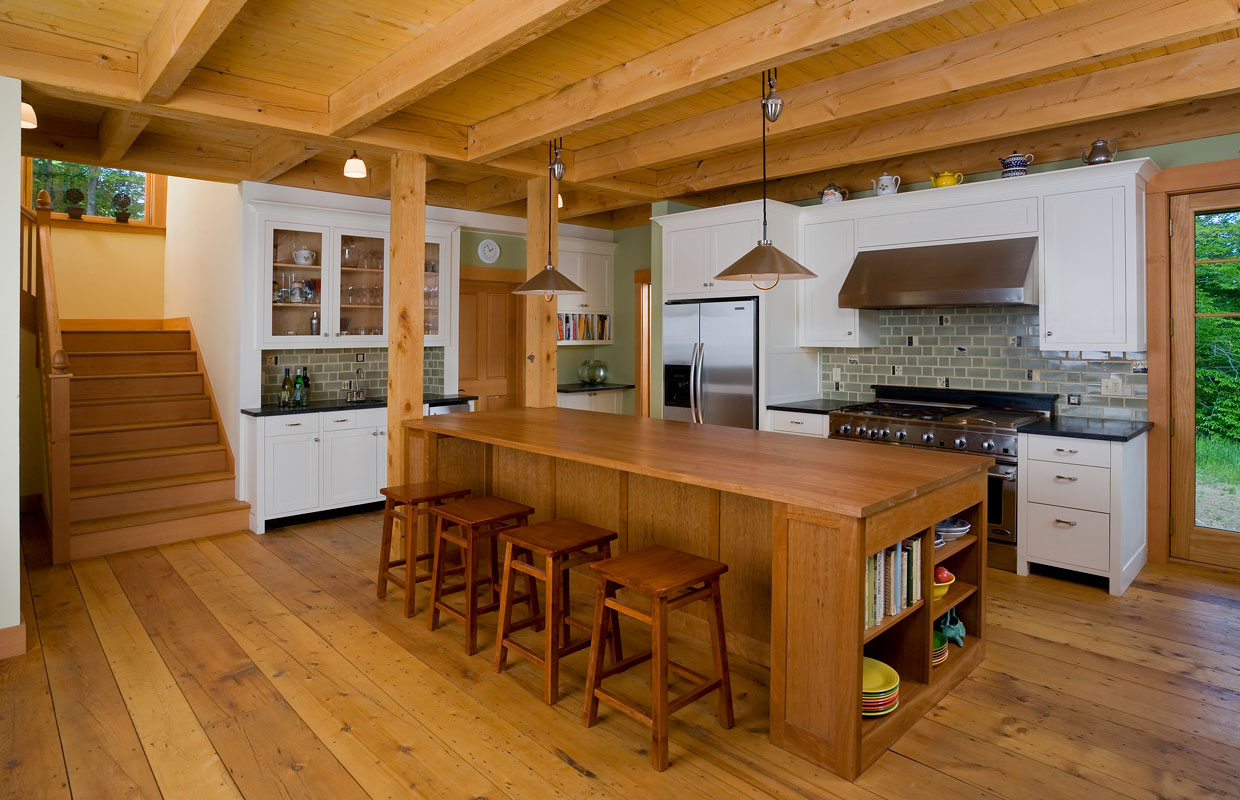 view into a large kitchen with a wooden island and staircase to the left