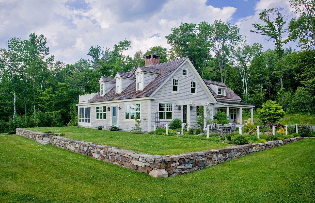 gray house with stone wall and green lawn