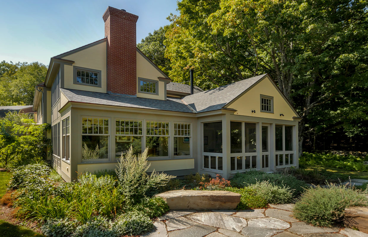 large cream house with a brick chimney and stone patio