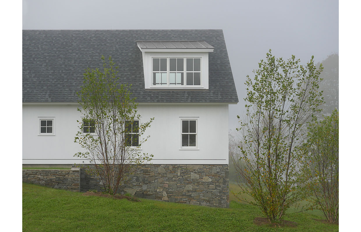 side of a white farmhouse in the fog with a stone foundation