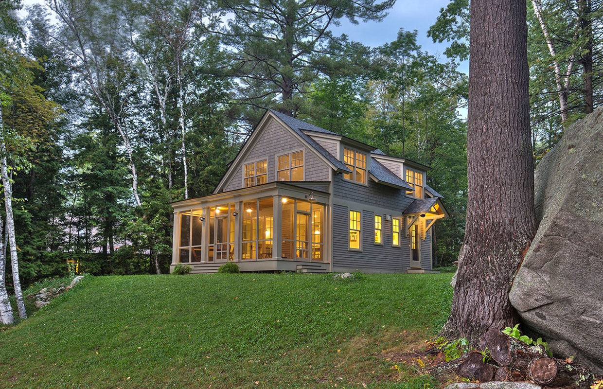 tan house at dusk in the woods with the lights on inside