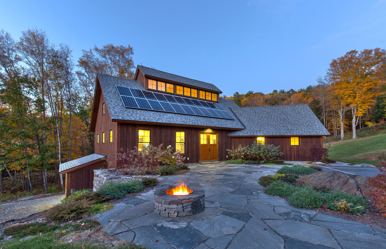 large barn at dusk with solar panels on the roof and a firepit