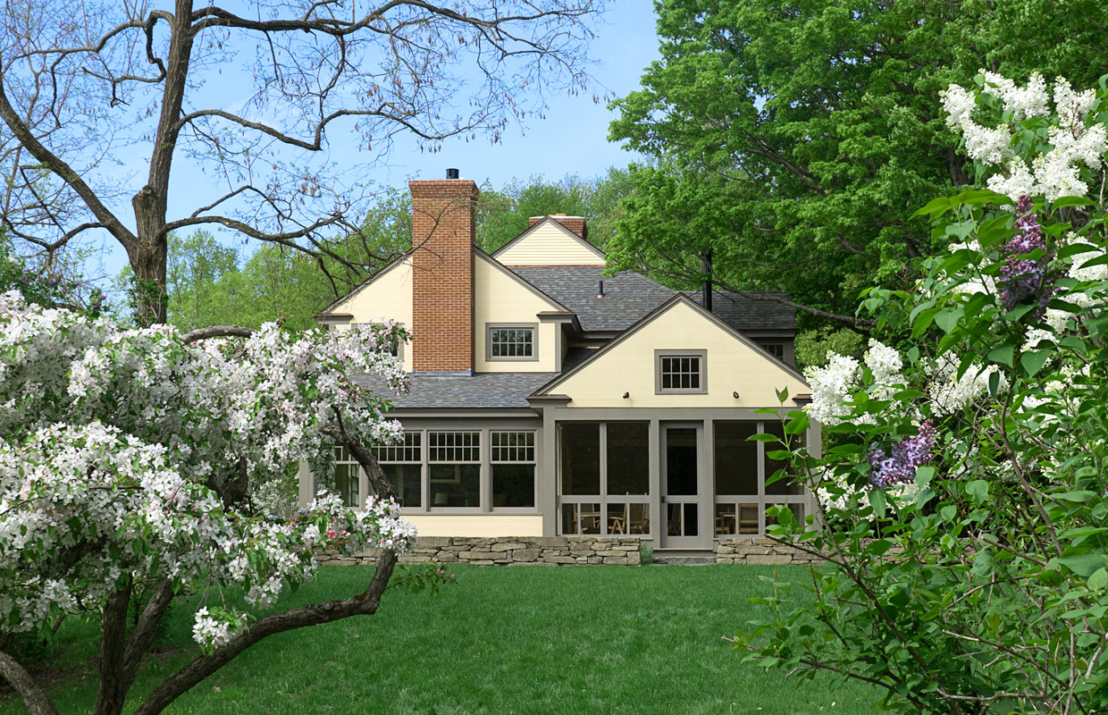 cream house with large windows and blossoming trees in the yard