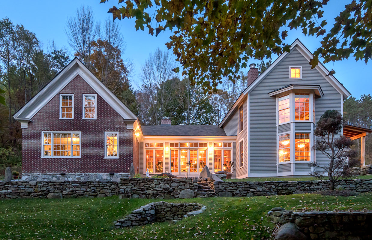 gray and brick house with a stone wall view from outside at dusk